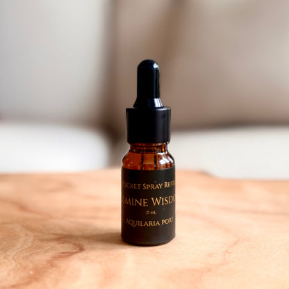 A small amber glass dropper bottle with a black cap stands on a light wood surface, with a softly blurred indoor background.