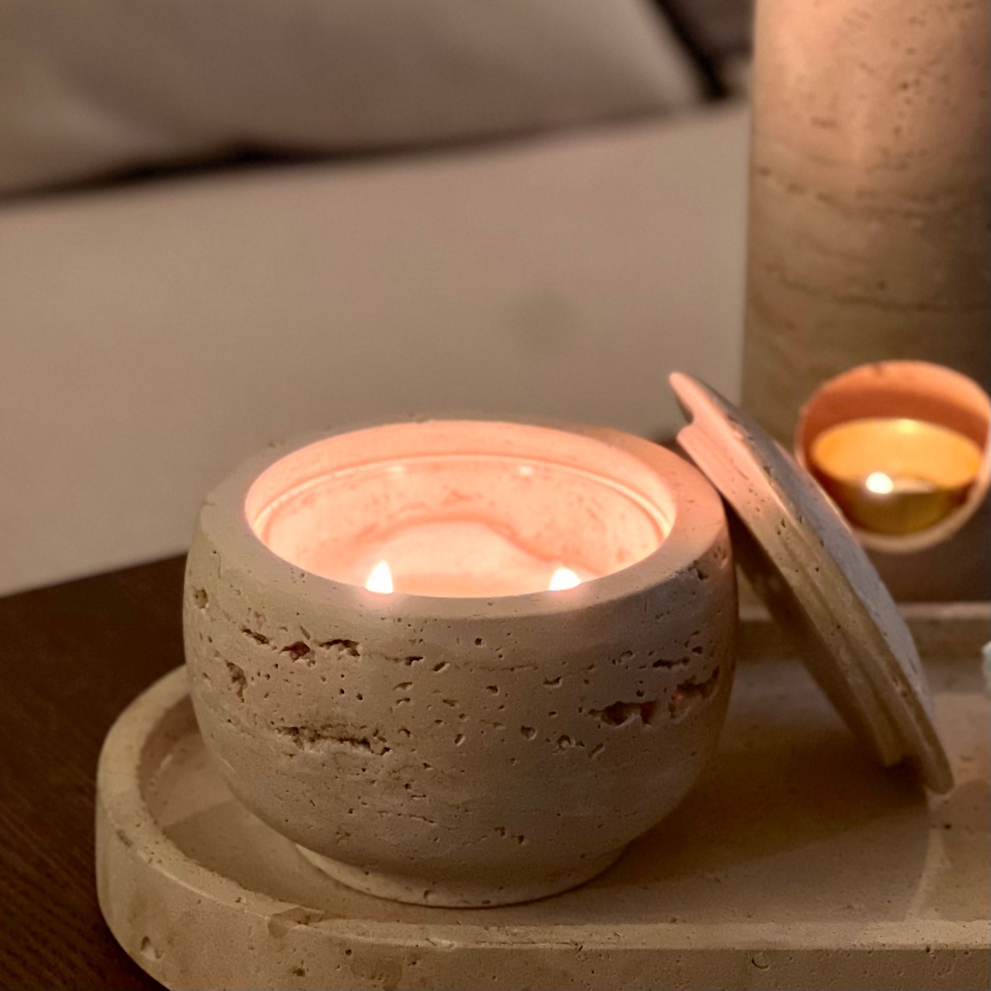 Travertine candle holder with a lit candle on a wooden surface