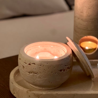 Travertine candle holder with a lit candle on a wooden surface