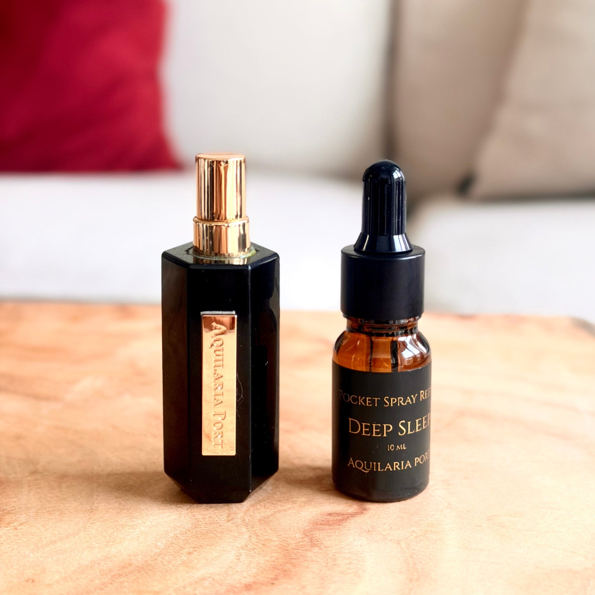 A black obsidian crystal atomiser and a 10ml dropper bottle of refill from Aquilara Port on a light wood surface with a blurred living room background. 