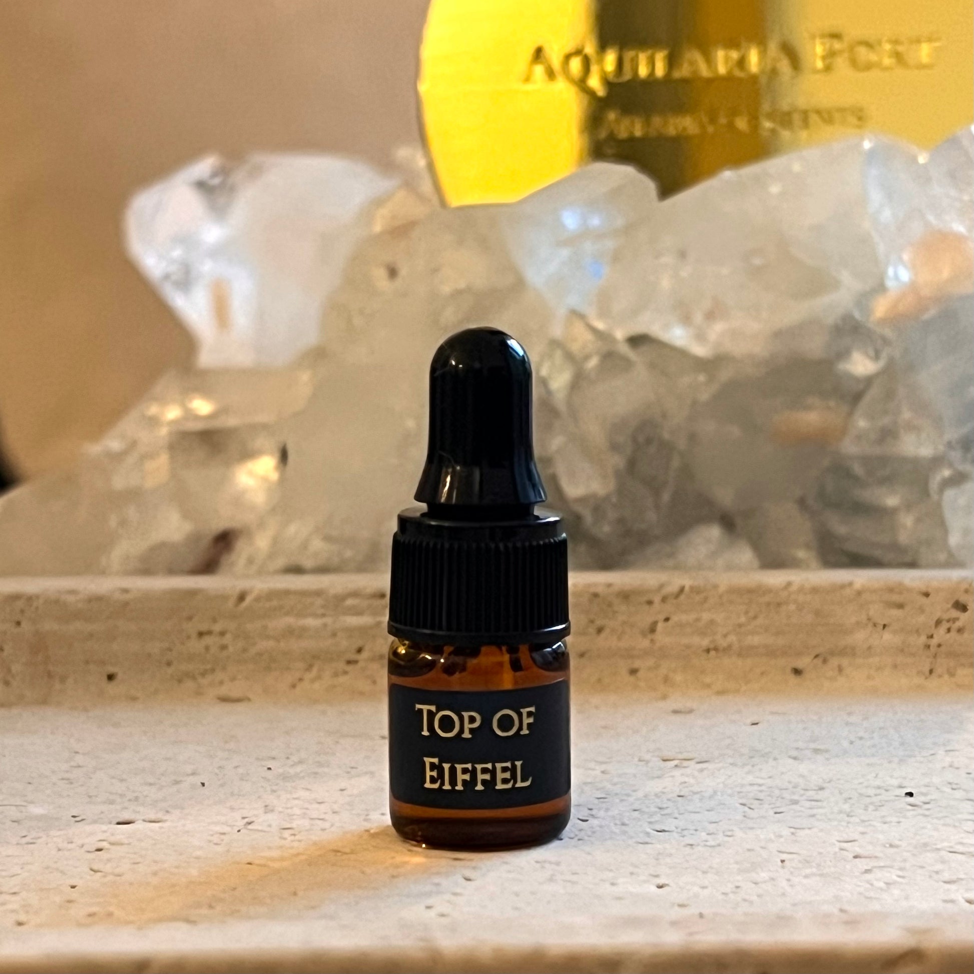 Bottle labeled 'Top of Eiffel' with crystals and a gold plaque in the background